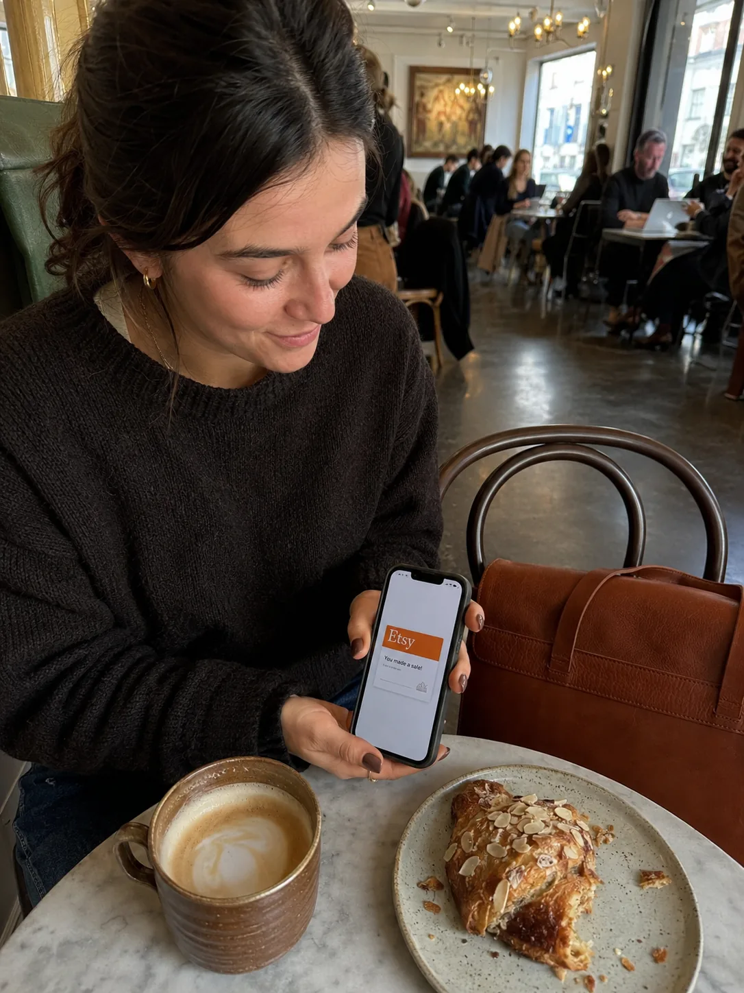 Seller checking an Etsy sale notification on her phone at a cafe table, quiet smile