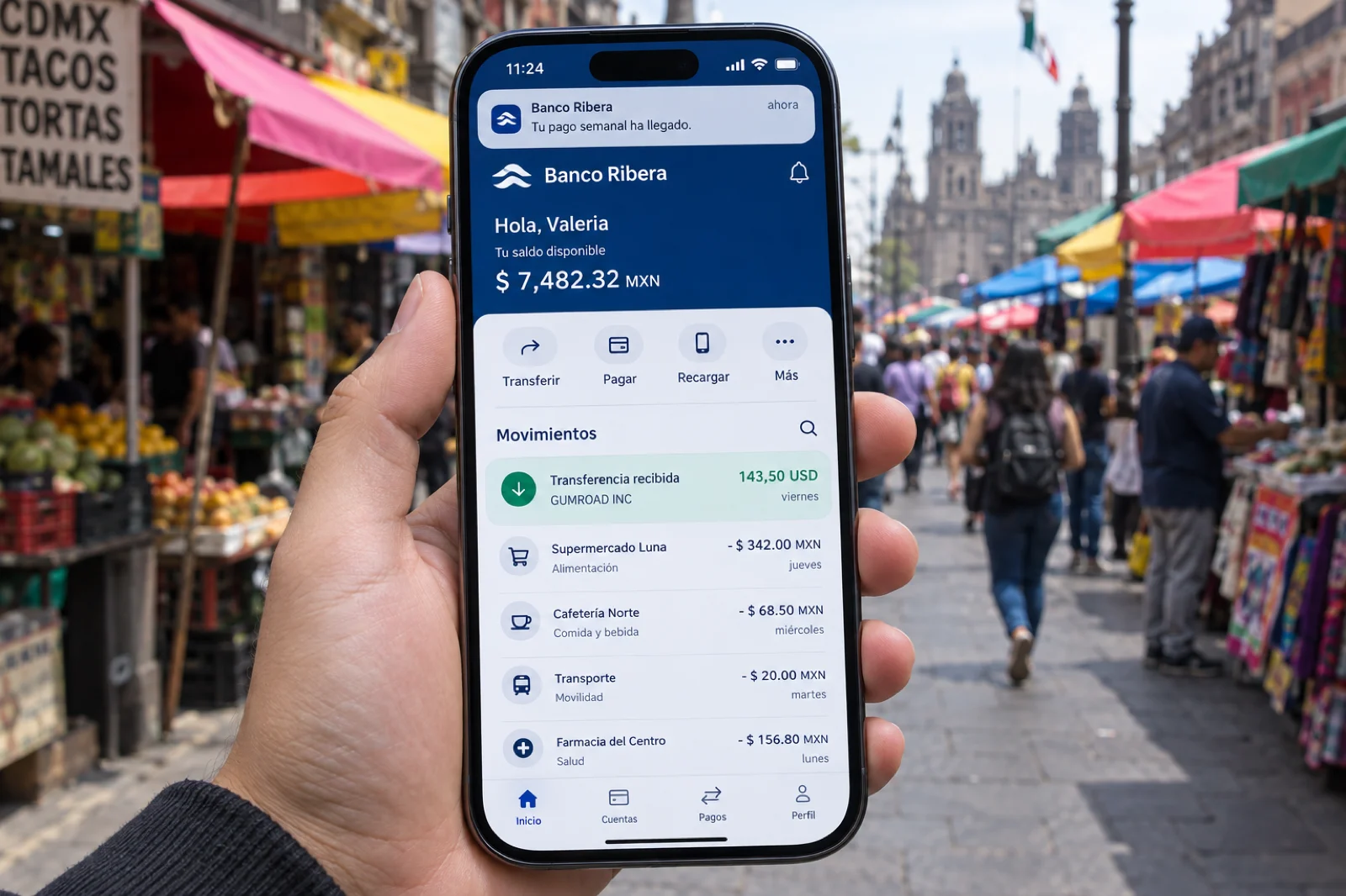 Mano sosteniendo un móvil en una calle de mercado en Ciudad de México; la app bancaria en español muestra una transferencia recibida de Gumroad de 143,50 USD un viernes y el aviso Tu pago semanal ha llegado