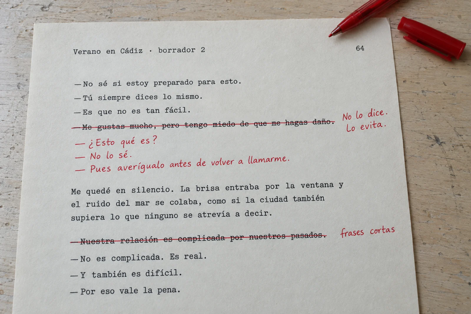 Página mecanografiada de 'Verano en Cádiz, borrador 2' con la línea 'Me gustas mucho, pero tengo miedo de que me hagas daño' tachada en rojo, la nota al margen 'No lo dice. Lo evita.' y el diálogo sustituto escrito a mano: '¿Esto qué es? No lo sé. Pues averígualo antes de volver a llamarme.'