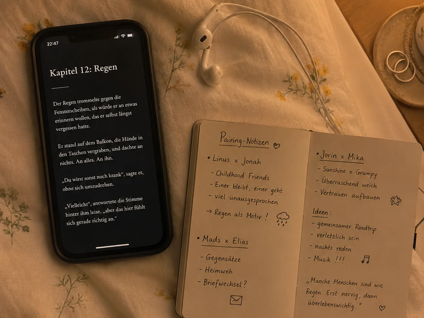 Ein Smartphone auf einer Bettdecke, auf dem ein deutschsprachiges Fanfiction-Kapitel mit der Überschrift Kapitel 12: Regen geöffnet ist, daneben Kopfhörer und ein kleines Notizbuch mit handschriftlichen Pairing-Notizen, warmes Lampenlicht.