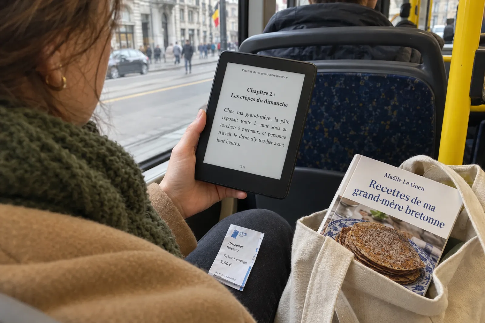 Dans un bus à Bruxelles, une passagère lit sur une liseuse le Chapitre 2 : Les crêpes du dimanche de Recettes de ma grand-mère bretonne, dont l’exemplaire broché de Maëlle Le Guen dépasse de son sac.