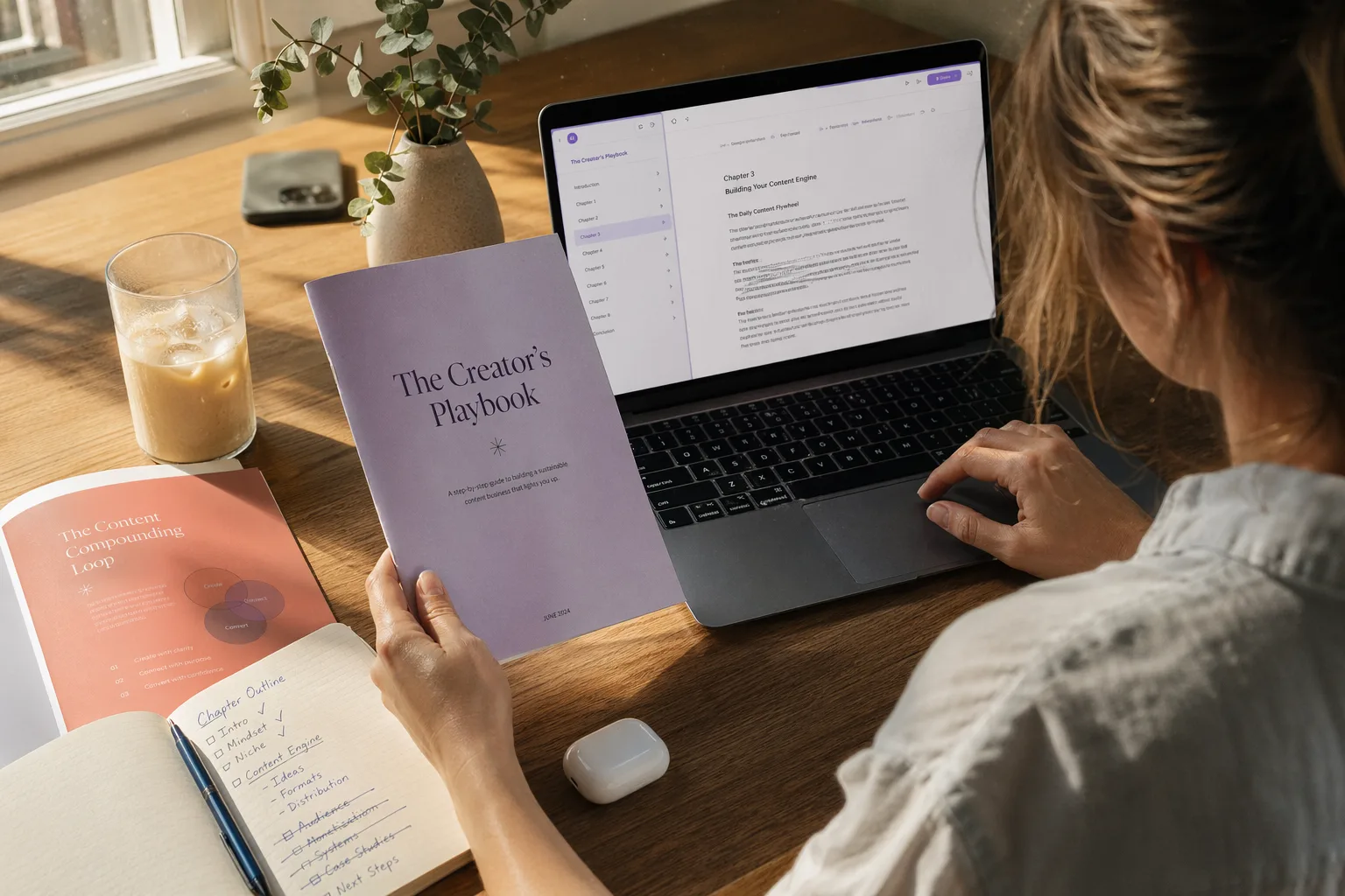 A solo founder at a bright home office creating a free AI PDF on a laptop. Beside the laptop is a printed PDF with a soft lavender cover, an open notebook with a rough outline, a glass of iced coffee, and a small succulent