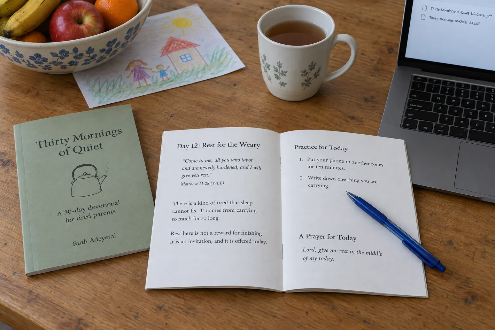 An open stapled devotional booklet on a kitchen table at Day 12: Rest for the Weary, quoting Matthew 11:28 from the World English Bible, Come to me, all you who labor and are heavily burdened, and I will give you rest, with a Practice for Today list (put your phone in another room for ten minutes; write down one thing you are carrying) and A Prayer for Today; beside it a closed sage-green copy titled Thirty Mornings of Quiet, A 30-day devotional for tired parents, by Ruth Adeyemi, a mug of tea, a child's drawing and a laptop listing Thirty-Mornings-of-Quiet_US-Letter.pdf and Thirty-Mornings-of-Quiet_A4.pdf