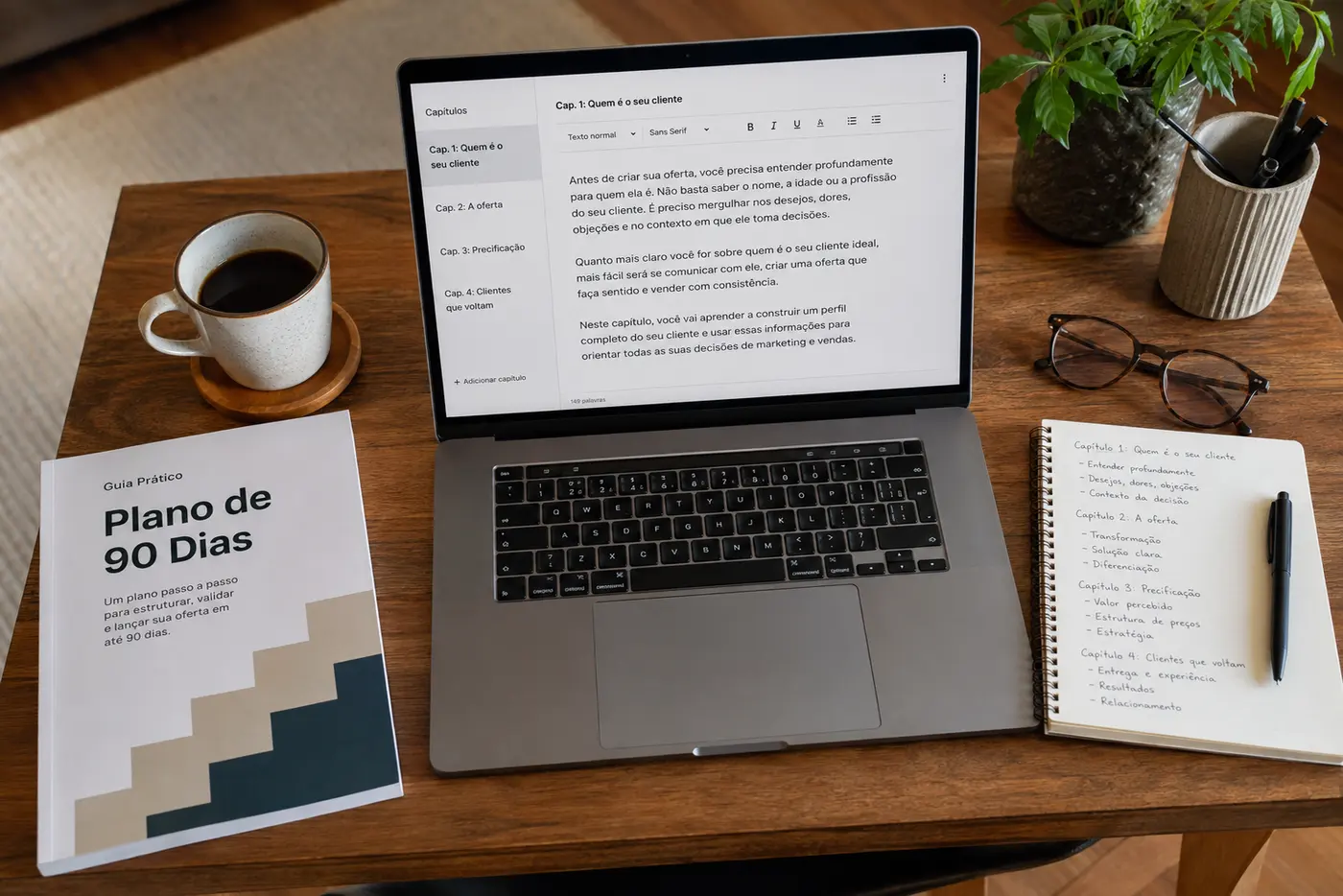 Mesa de madeira com um notebook exibindo um aplicativo de escrita em português, com a lista de capítulos de um guia prático e o texto do primeiro capítulo sobre definir o cliente ideal. Ao lado, um guia impresso com o título Plano de 90 Dias, uma xícara de café, óculos e um caderno com o esboço dos capítulos escrito à mão.